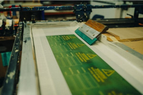 Screen printing green labels for clothing at JammyThreads, with squeegee and press frame.