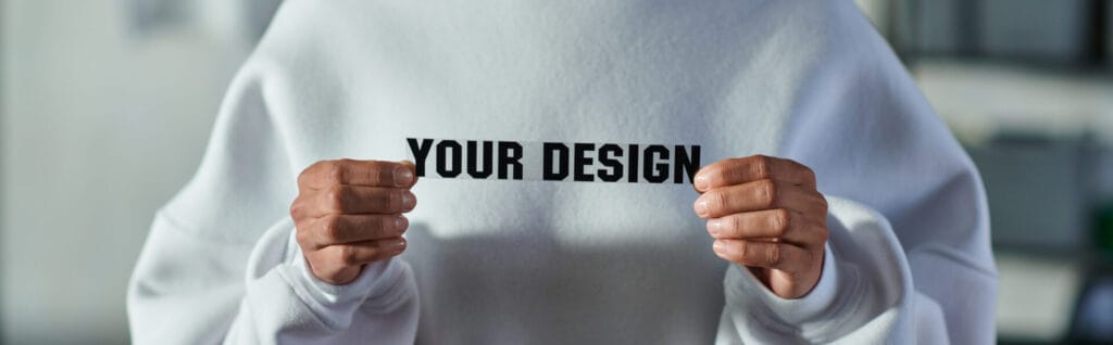 Person holding YOUR DESIGN paper cutout over a white sweatshirt for Jammy Threads.